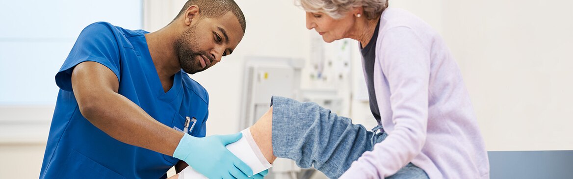 En mandlig sygeplejerske, der skifter bandagen på en patient.