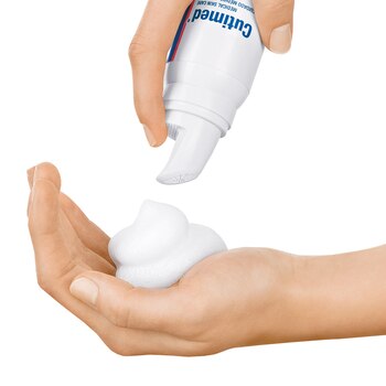 We zien in close-up hoe de ene hand de spray gebruikt en een beetje Cutimed ACUTE Crèmemousse in de palm van de andere hand doet.